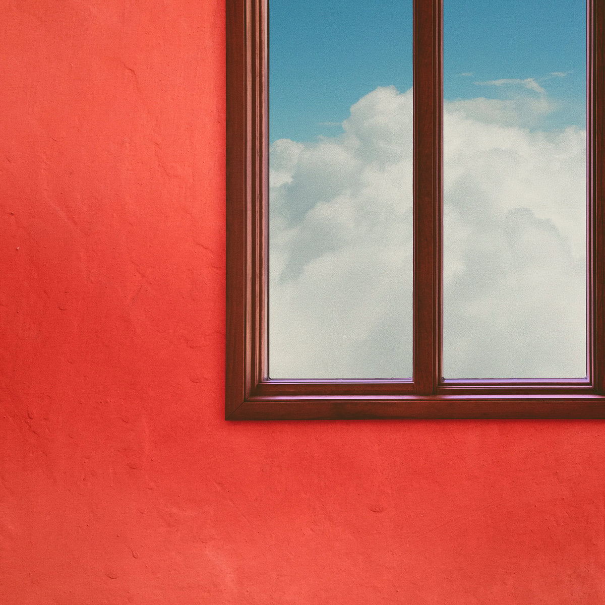 A window framed in a red wall, showcasing a blue sky and white clouds.