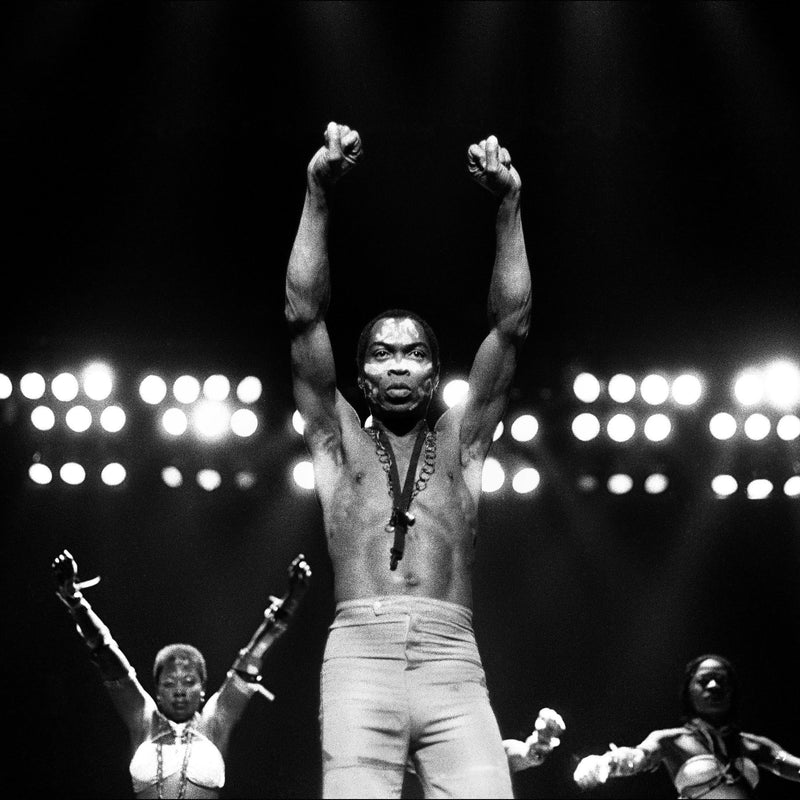 A monochrome photograph capturing a man (Fela Kuti) on stage, with dramatic lighting highlighting his presence