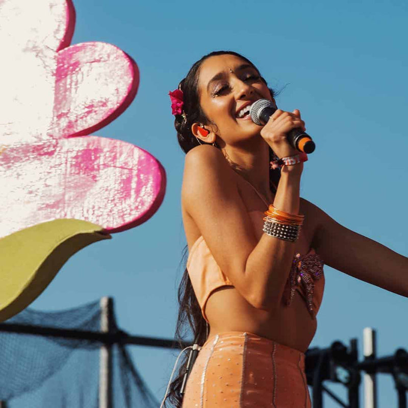 A performer in an orange outfit singing into a microphone with a flower backdrop.