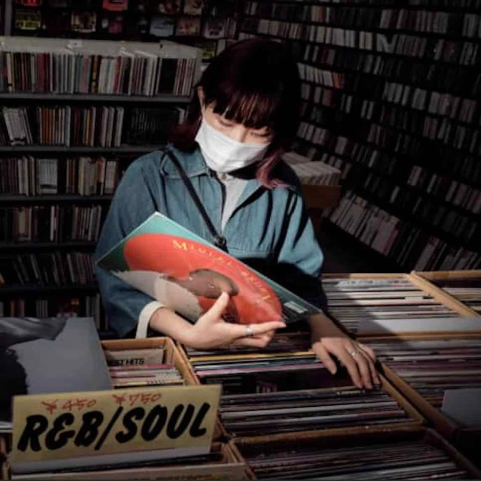 Person holding a vinyl record in a music store with racks of CDs and records.