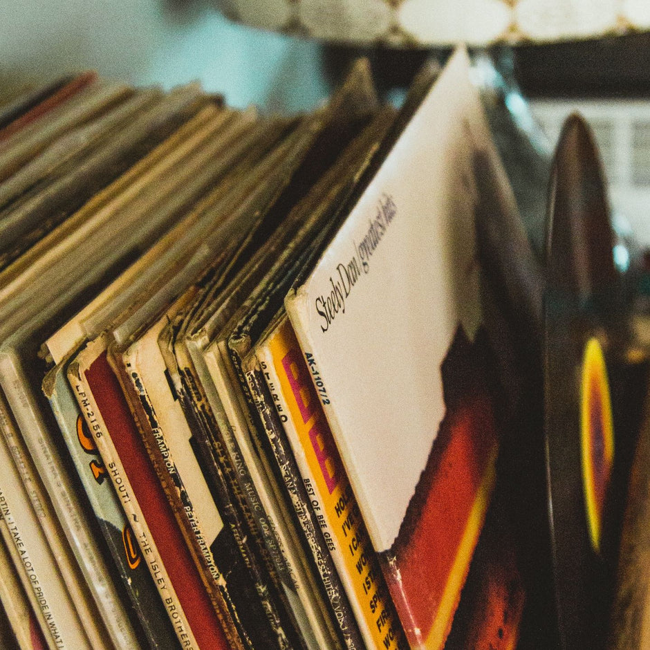Row of vinyl record sleeves on a shelf, with a record player in the background.