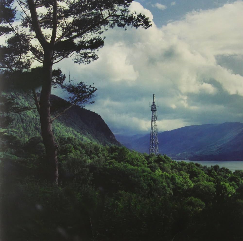 A serene view of a tower beside a tranquil lake, surrounded by lush green trees under a clear blue sky