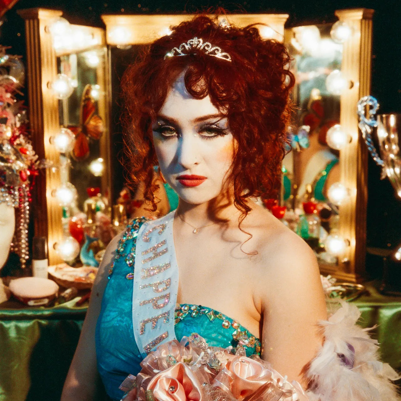 A woman standing next to a dressing table with a tiara on her head 