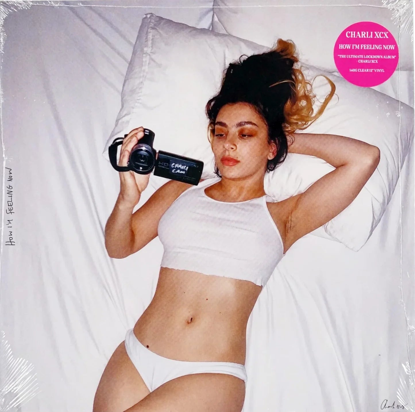 Charli XCX - How I'm Feeling Now Vinyl Record

Woman in white sports bra and shorts holding a camera on a bed, with 'Charlii' branding.