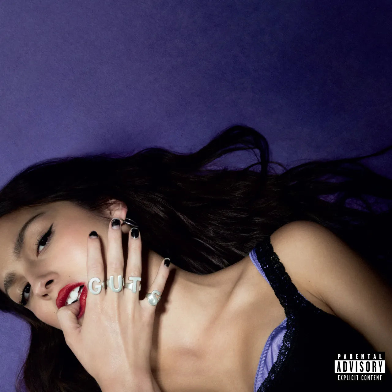 Olivia Rodrigo lying down with her hands on display with the ring on the hand spelling G U T S